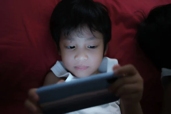 A cute Asian boys lying on their mobile phones in a dark bedroom. Addict Playing Smartphone.Nomophobia in children.
