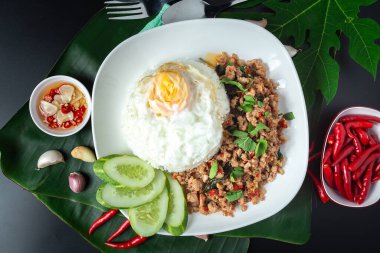 Tayland sokak yemeği, fesleğenli pilav, kıyma, sahanda yumurta ve siyah masada dilimlenmiş salatalık..