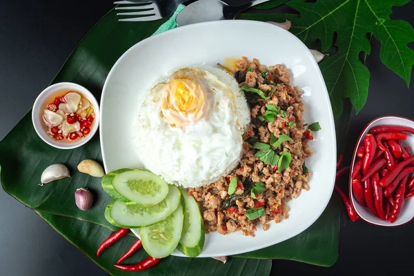 Thai street food, basil fried rice, minced pork, fried egg and sliced cucumber on a black table.