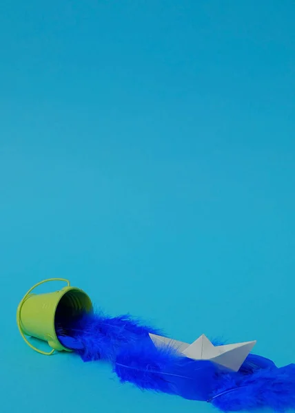 緑色のバケツから青い羽をこぼし 明るい青色の背景に白い紙で作られたボート テキスト空間 こぼれる 排水する 創造的 ミニマルスタイル — ストック写真