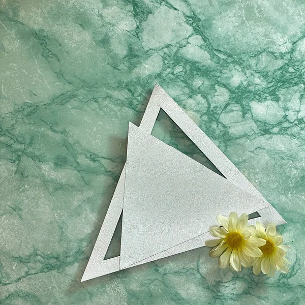 Silver triangle and frame, two marguerite daisy flowers on a green marble background. Text space. Top view. Minimal style.