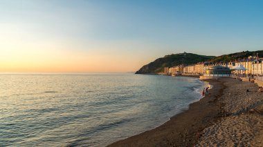 Aberystwyth, Ceredigion, Wales, UK - May 25, 2017: Evening view over the North Beach and the Marine terrace, with people on the beach and the Cliff Railway in the background clipart
