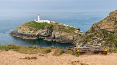 Holyhead, Anglesey, Gwynedd, Galler, İngiltere - Haziran 08, 2018 - Arka planda Güney Yığını Deniz Feneri ile 'Tehlike Uçurumları' nı (Galce & İngilizce) İmzala