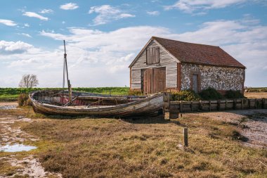 Thornham, Norfolk, İngiltere, İngiltere - 24 Nisan 2019 Thornham Old Harbour 'da yanında ahşap yelkenli teknesi olan eski bir taş ahır
