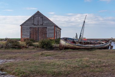 Thornham, Norfolk, İngiltere, İngiltere - 24 Nisan 2019 Thornham Old Harbour 'da yanında ahşap yelkenli teknesi olan eski bir taş ahır
