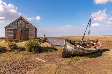 Thornham, Norfolk, İngiltere, İngiltere - 24 Nisan 2019 Thornham Old Harbour 'da yanında ahşap yelkenli teknesi olan eski bir taş ahır