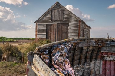 Thornham, Norfolk, İngiltere, İngiltere - 24 Nisan 2019 Thornham Old Harbour 'daki eski taş bir ahır önünde ahşap bir yelkenli teknesi var.