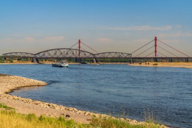 Duisburg, Kuzey Ren-Westfalia, Almanya - 07 Ağustos 2018: Arkasında Beeckerwerther Köprüsü ve Haus-Knipp Demiryolu Köprüsü olan Ren Nehri 'nde kavrulmuş bir çayır