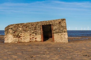 Kuzey kıyısı Caister-on-Sea, Norfolk, İngiltere - kumsalda eski bir sığınak ve arka planda rüzgar türbinleri ile