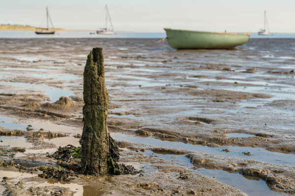 A wooden stake in the Oare Marshes at low tide near Faversham, Kent, England, UK - with some boats and the Isle of Sheppey in the background
