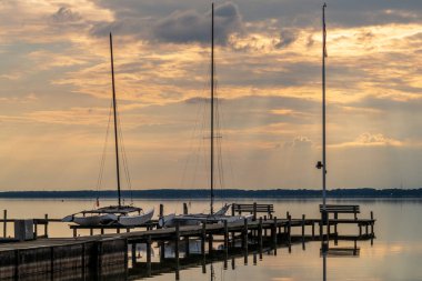 Akşam güneşi bulutların arasından parlayan bir iskelede bir bank ve Fluegelhorst, Aşağı Saksonya, Almanya 'daki Steinhuder Meer' de bir manzara.