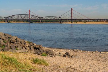 Duisburg, Kuzey Ren-Westfalia, Almanya - 07 Ağustos 2018: Arkasında Beeckerwerther Köprüsü ve Haus-Knipp Demiryolu Köprüsü olan Ren Nehri 'nde kavrulmuş bir çayır