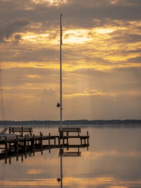 Akşam güneşi bulutların arasından parlayan bir iskelede bir bank ve Fluegelhorst, Aşağı Saksonya, Almanya 'daki Steinhuder Meer' de bir manzara.