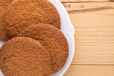 Birkaç lezzetli yuvarlak Amerikan kurabiyesi seramik beyaz bir tabakta, yakın planda, ahşap bir masada..