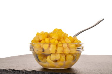 Cam bir fincan tabağında parlak sarı mısır taneleri beyaz bir arka planda izole edilmiş, makro bir taş üzerinde..