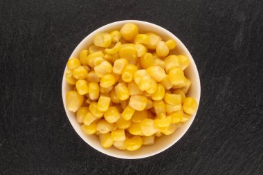 Parlak sarı mısır tanecikleri beyaz bir çay tabağında kayrak taşı, makro, üst manzara.