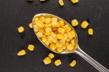 Parlak sarı mısır tanecikleri, kayrak taşı üzerinde metal kaşık, makro, üst manzara..