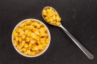Parlak sarı mısır tanecikleri, beyaz bir fincan tabağında metal bir kaşık, makro, üst manzara..