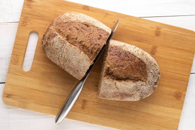 Bir somun ekmek, kokulu karabuğday ekmeği, tahta bir kesme tahtasının üzerinde metal bir bıçak, yakın plan, ahşap bir masa, üst görüş..