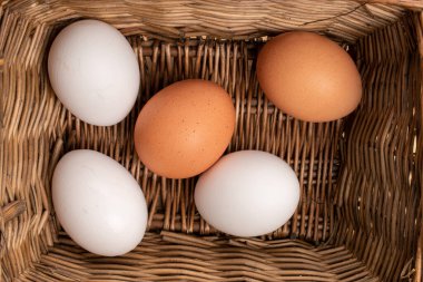 Sarmaşıktan örülmüş sepetteki bej ve beyaz taze organik tavuk yumurtaları..