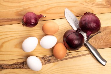Birkaç bej ve beyaz taze organik tavuk yumurtası, üç soğan ve bir metal bıçak..