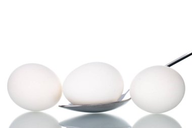 Metal kaşıklı üç beyaz tavuk yumurtası, yakın plan, beyaz üzerine izole edilmiş..