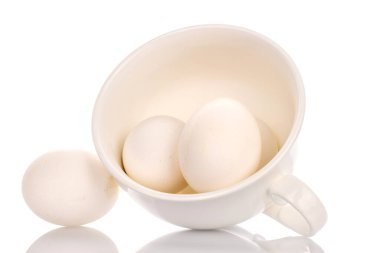 Beyaz seramik bardaklı üç beyaz tavuk yumurtası, yakın plan, beyaz arka planda izole edilmiş..