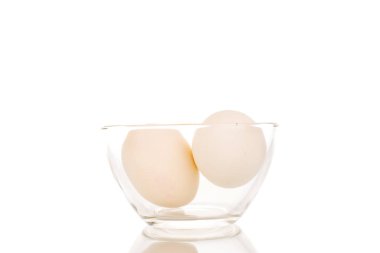 Cam bir tabakta iki beyaz tavuk yumurtası, makro, beyaz arka planda izole edilmiş..