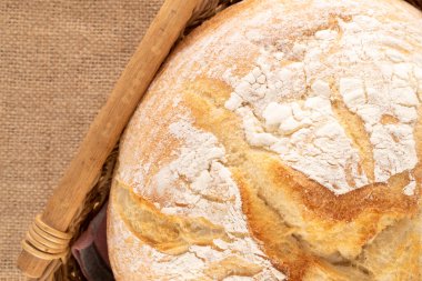 Çuval bezeli sepetin içinde bir somun taze kokulu buğday ekmeği, yakın plan, üst manzara..