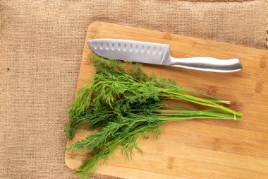 Bir demet taze, yeşil dereotlu bıçak ve bambu kesme tahtasıyla çuval bezi, makro, üst manzara..