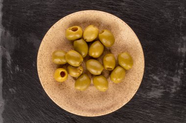 Çeşitli baharatlı organik turşulu yeşil zeytinler açık seramik bir tabağın üzerinde uzanır..