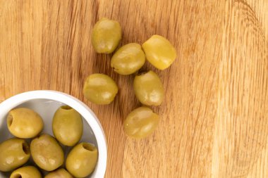 Birkaç baharatlı organik turşulu yeşil zeytin, beyaz bir seramik tabağın üzerinde doğal ahşap arka planda, üst manzarada..