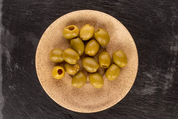 Çeşitli baharatlı organik turşulu yeşil zeytinler açık seramik bir tabağın üzerinde uzanır..