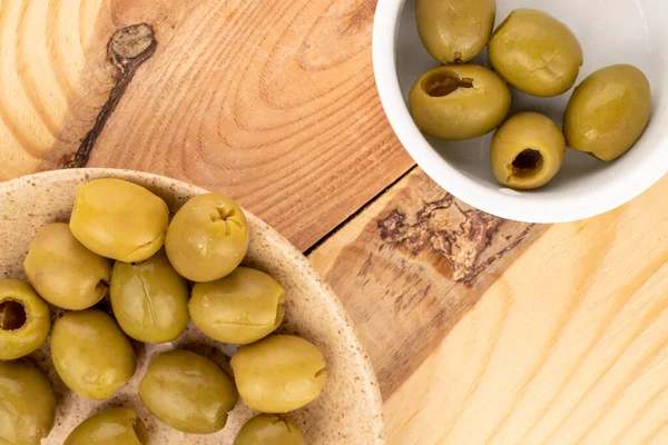 Çeşitli baharatlı organik turşulu yeşil zeytinler ışık ve beyaz seramik tabaklar üzerine uzanır..