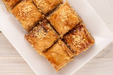 Klasik tatlı baklava, beyaz seramik bir tabak ile ahşap bir masa, makro, üst görünüm.