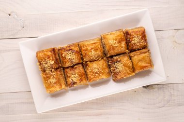 Klasik tatlı baklava, beyaz seramik bir tabak ile ahşap bir masa, makro, üst görünüm.