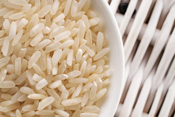 Beyaz organik pirinç, sarmaşık hasırında beyaz bir tabakta, yakın plan, üst manzara..