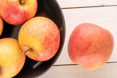 Tahta bir masanın üzerinde siyah seramik plakalı birkaç kırmızı organik elma, yakın plan, üst manzara..