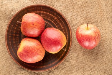 Çamur bir plaka üzerinde kırmızı organik elmalar, jüt kumaş, yakın çekim, üst görünüm.