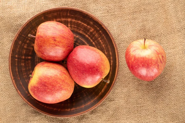 Çamur bir plaka üzerinde kırmızı organik elmalar, jüt kumaş, yakın çekim, üst görünüm.