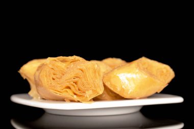 Seramik bir tabakta, makroda, siyah bir arka planda izole edilmiş birkaç dilim bal baklavası..