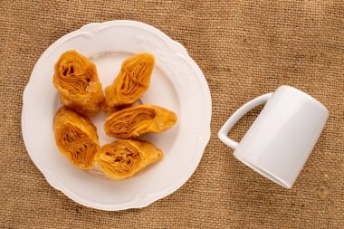 Beyaz seramik tabaklı birkaç parça bal baklavası ve çuval bezinde bir fincan, yakın plan, üst manzara..