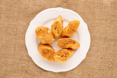 Çuval bezinde beyaz seramik tabağı olan birkaç tatlı bal baklavası..