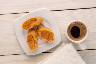 Beyaz seramik tabağı olan üç parça bal baklavası ve ahşap bir masada bir fincan kahve, yakın çekim, üst manzara..