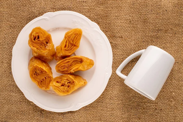 Beyaz seramik tabaklı birkaç parça bal baklavası ve çuval bezinde bir fincan, yakın plan, üst manzara..