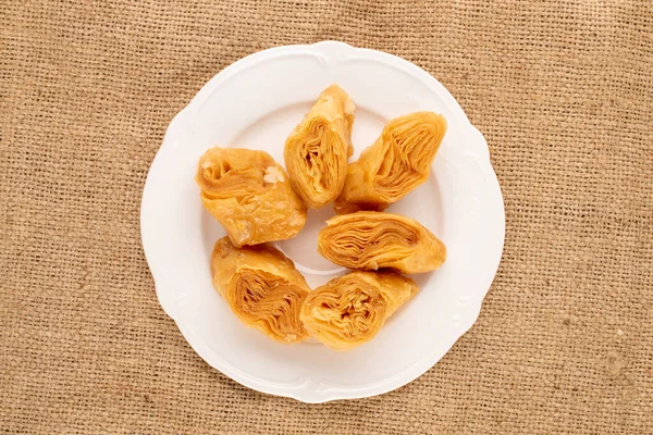 Çuval bezinde beyaz seramik tabağı olan birkaç tatlı bal baklavası..