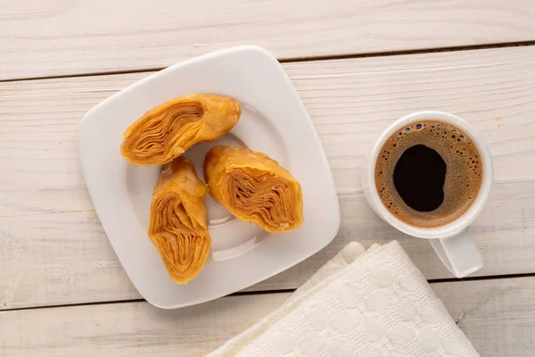 Beyaz seramik tabağı olan üç parça bal baklavası ve ahşap bir masada bir fincan kahve, yakın çekim, üst manzara..