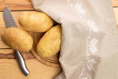 Üç taze, soyulmamış, organik sulu, patates, yuvarlak bir bambu tepside, metal bir bıçak ve keten peçeteyle, ahşaptan yapılmış bir masanın üzerinde, üst görünüm.