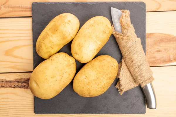 四个新鲜的 没有剥皮的 有机多汁的土豆 用金属刀包在黄麻餐巾上 放在用天然木料做的桌子上 顶部看 — 图库照片