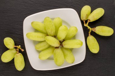 Beyaz seramik tabağı olan bir demet çekirdeksiz üzüm, kayrak taşı, yakın plan, üst görüş.